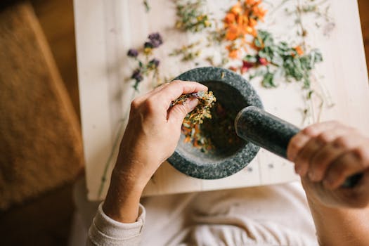 Top view of hands grinding dried herbs using a mortar and pestle on a wooden table.